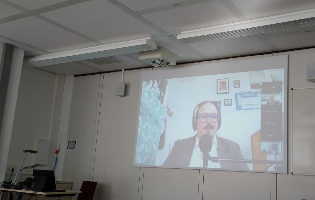 speaker of a conference talk, projected to the wall of a seminar room